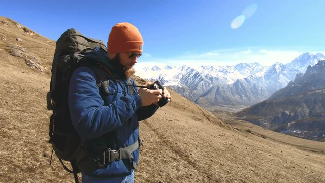Portrait of a happy bearded traveler photographer in sunglasses and a hat with a reflex camera in his hands and taking pictures against the background of the mountains. Photo travel concept