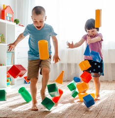 little brother and sister run around the room spreading legs toy raznocvetnye plastikovye blocks.