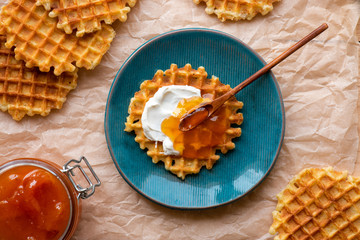 Belgian waffles with jam on a blue plate, flat lay, top view. Delicious breakfast or lunch with homemade Belgian waffles.