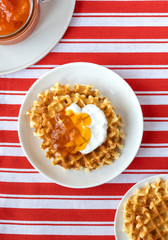 Belgian waffles with jam on a red plate, flat lay, top view. Delicious breakfast or lunch with homemade Belgian waffles.