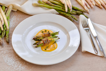 asparagus wrapped in grilled bacon with sauce on a white plate