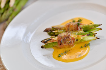 asparagus wrapped in grilled bacon with sauce on a white plate