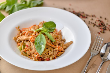 pasta with chicken and vegetables decorated with basil on a white plate