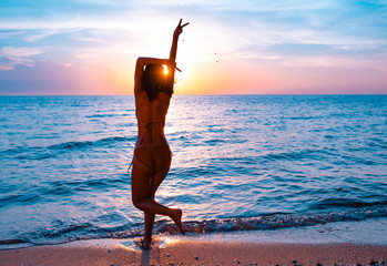 Silhouette of a beautiful, slim girl who jumps and Hold two fingerson a background of a sunset on the beach