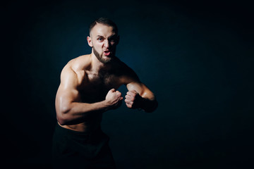 Low key portrait of muscular shirtless man at dark background