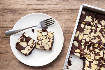 Homemade sliced brownies on white plate with fork. Top view on wooden table.