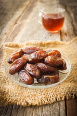 Dried date fruit on glass plate over wooden table. With glass of tea is background. Warm color tone.