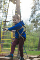 A little boy is training in a rope park. The child climbs the obstacle course. Active recreation in the park in the fresh air.
