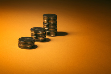 Three stacks of golden coins sitting on a soft orange surface casting small shadow – Money arranged in piles for better organizing and accounting – concept image for investment and financial growth