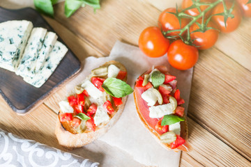 Traditional Italian bruschetta with blue cheese, feta, tomatoes, basil leaves, jamon on a wooden background.