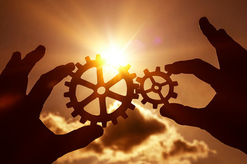 gears in the hands of people on the background of the evening sky. the mechanism of interaction.