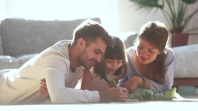 Happy family parents drawing with cute child daughter on floor