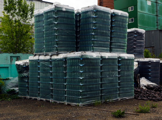 Finished products of clean bottles are packed in pallets. Racks with bottles are in  abandoned area near  glass factory near  forest.
