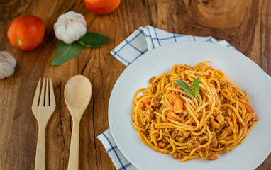 Spaghetti with tomato sauce in a white plate on a wooden background.