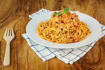 Spaghetti with tomato sauce in a white plate on a wooden background.