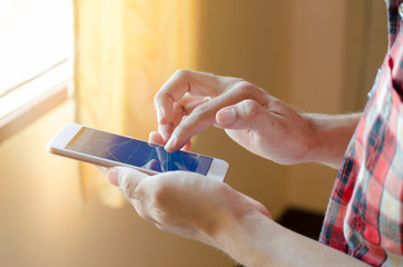 Men wearing a red shirt with a Scottish pattern are touching screen his smartphone.