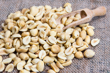 Peeled peanuts and wooden scoops are on burlap