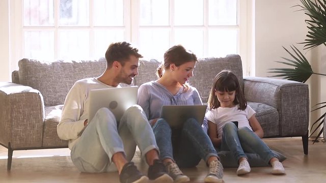 Happy modern family sit on floor talking using devices