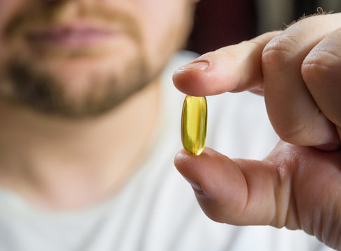Man's hand holding omega 3 fish oil capsula