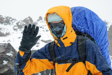Portrait of a tourist (hiker) with a backpack in bad weather in the mountains. Heavy snowstorm. Face closed with a windproof mask. Extreme clothing