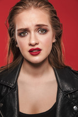 Beautiful young sad emotional woman with bright makeup red lipstick posing isolated over red wall background.