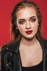 Beautiful young amazing woman with bright makeup red lipstick posing isolated over red wall background.