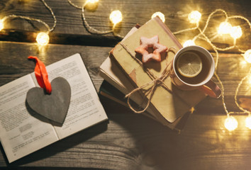 Holidays mood photo. Christmas lights and hot tea mug. Book for cosy evening. Sweet gingerbread and...