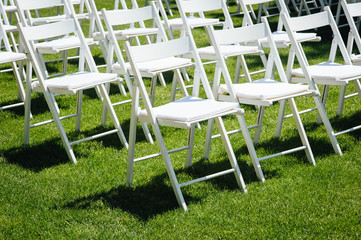 Rows of white folding chairs on lawn before a wedding ceremony in summer