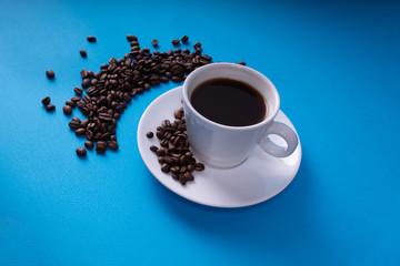 White cup with a drink set on a saucer strewn with coffee beans
