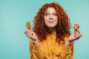 Portrait of happy redhead woman 20s smiling and eating sweet cookies