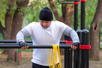 Fototapeta premium Street workout of a young man in the early Sunny morning. The man is preparing to perform a power load on the simulator and rubs sports magnesia.