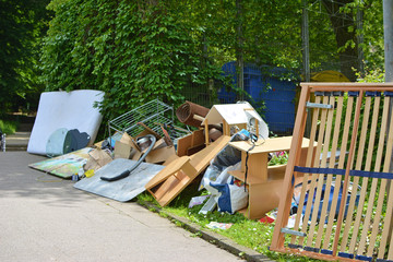 Bulky waste including old furniture, vacuum cleanerlying on grass next to street pavement