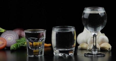 Alcohol drink vodka in shot glasses. Background with vegetables