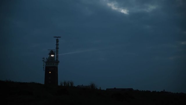 Shining lighthouse on the coast of the island in the evening. The light beam is well visible. No people.