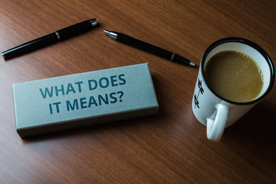 Word writing text What Does It Means question. Business photo showcasing asking meaning something said and do not understand Upper close view two ball point pens case set coffee cup lying wooden table