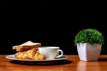 Coffee and bread croissants on the wooden and background black
