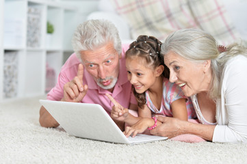 Grandparents with her granddaughter using laptop at home 