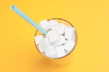 Top view of sugar cubes. A clear glass filled with sugar cubes on a yellow background. Minimal color still life photography. Copy space for text.