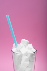 Glass full of white sugar cubes on pink background. Concept of unhealthy diet. Copy space for text.