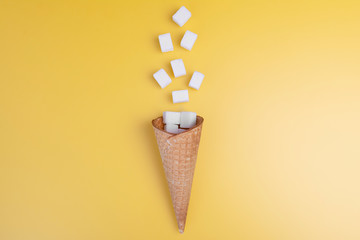 Flying sugar concept. Flying sugar cubes from ice cream cone on yellow background. Copy space for...