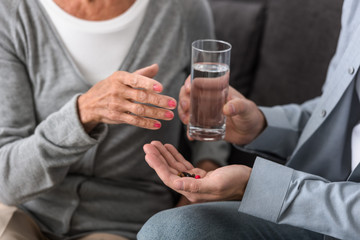cropped view of man giving to senior mother glass of water and medicine