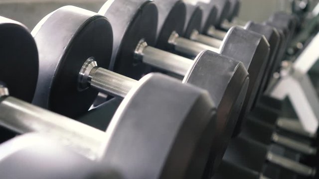 Dolly shot of dumbbells and barbells row in modern sport club gym
