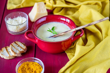 Cheese cream soup on a red wooden background. White bread croutons. Ingredients.