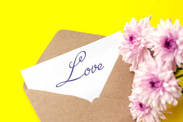 Love envelope and letter with written word love with pink chrysanthemum flowers on bright yellow bacground.