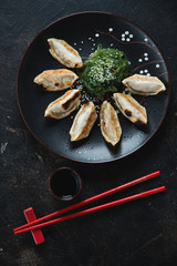 Gyoza dumplings with chuka salad, soy sauce and chopsticks, flatlay on a dark brown stone background