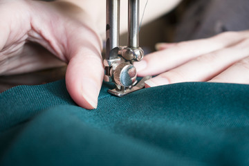 Young woman on her sewing process, women's hands behind her working on sewing machine. Closeup side