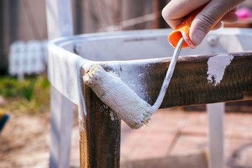 Woman hand with paint roller painting chair outside.