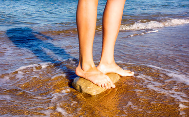 Woman bare feet standing on the stone in the sea.