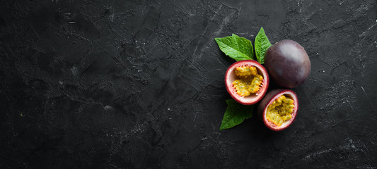 Passion fruits with leaves on a black background. Tropical Fruits. Top view. Free space for text.