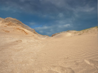 Blue cloudy sky over sand dunes. Sand pattern.